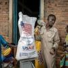 A Burundian government official speaks with newly arrived Congolese refugees while weighing a sack of rice from the final batches delivered by the now-dismantled United States Agency for International Development