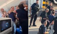Moment raging British Airways passenger is restrained by brave female flight attendant after trying to attack other travellers - before being escorted off plane by armed police