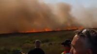 Farmer desperately shovels soil on blackened, smoking earth as wildfire rages