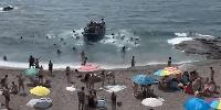 WATCH: Beachgoers flee as dozens of migrants leap from boat and charge ashore at tourist hotspot