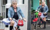 Suzy Eddie Izzard, 64, sports a pleated mini-skirt and towering knee-high boots as she cycles through Notting Hill without a helmet