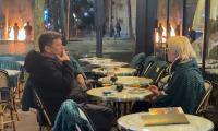 Keep calm and carry on: Unfazed French diners enjoy a drink at Parisian cafe during riots as fire burns in the background